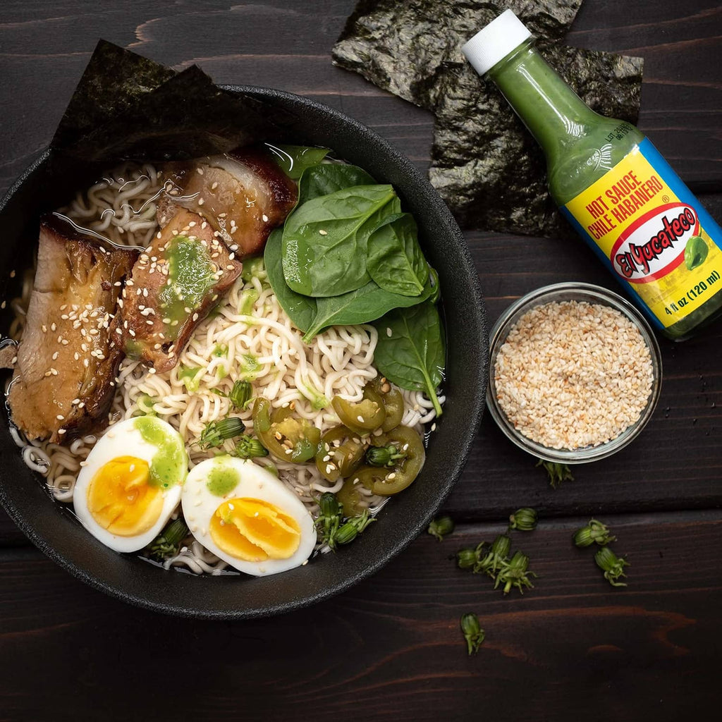 El Yucateco green habanero hot sauce bottle beside a noodle bowl with eggs