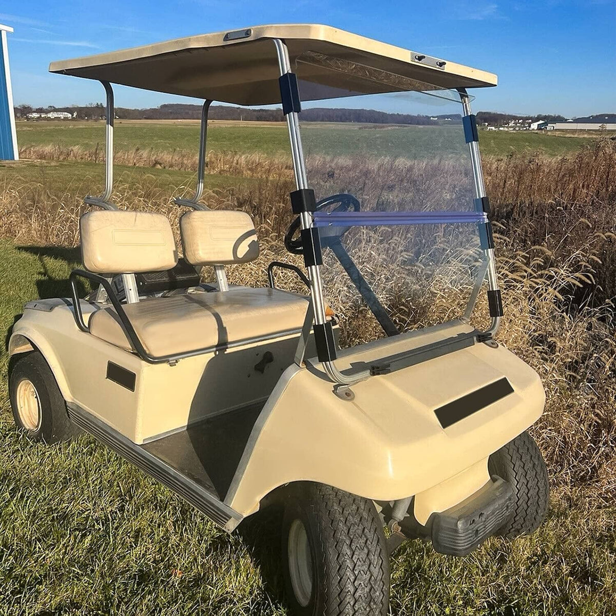 Clear folding golf cart windshield with black frame, angled side view on beige cart
