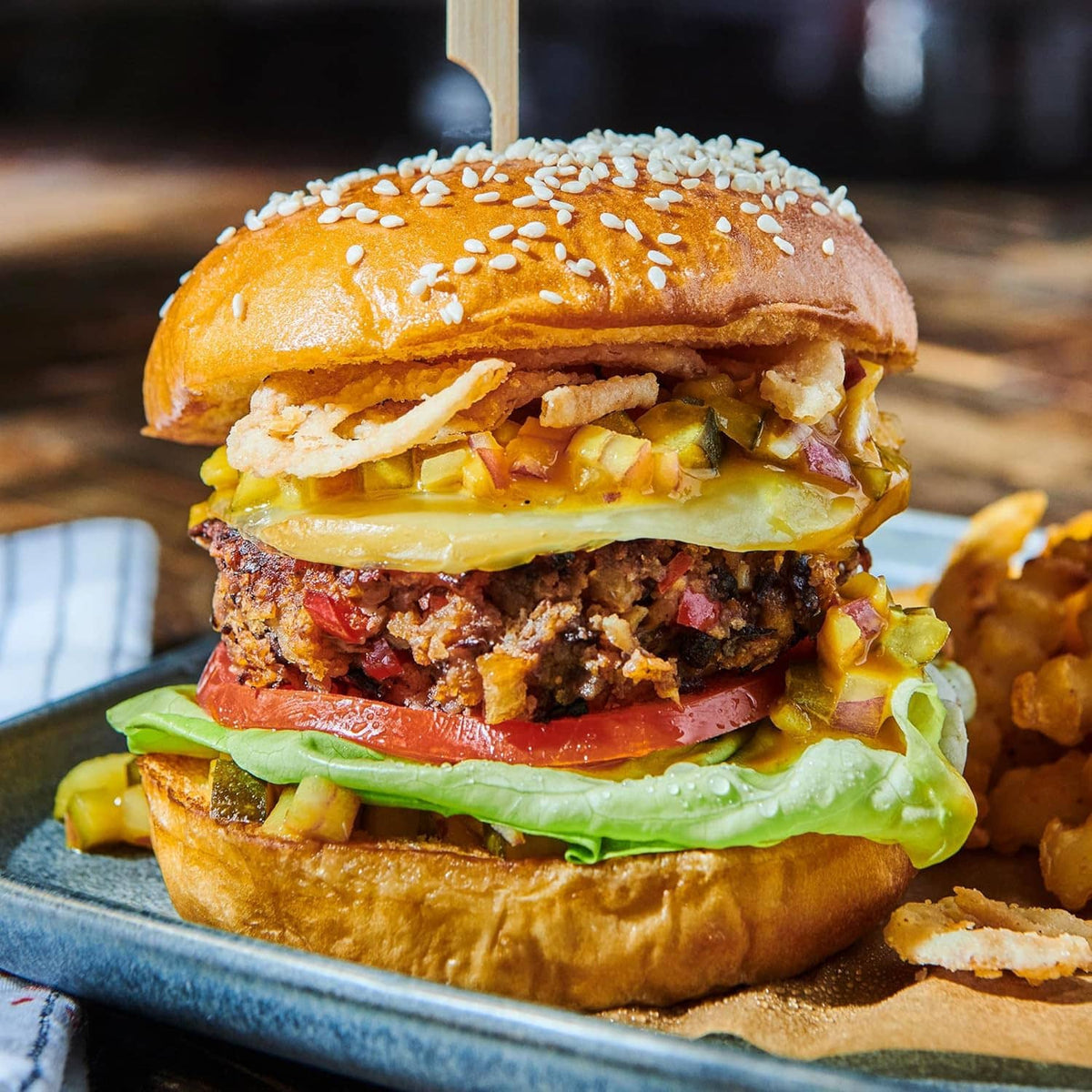 Burger topped with crispy fried onions, cheese, vegetables, and sesame bun on a plate