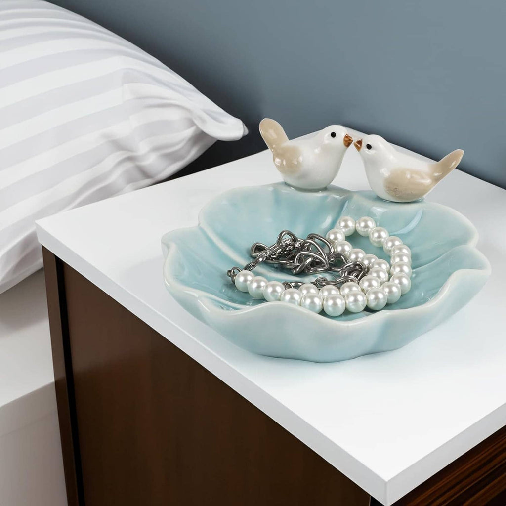 Ceramic lotus leaf jewelry tray with two white bird ring holders holding pearl bead bracelets