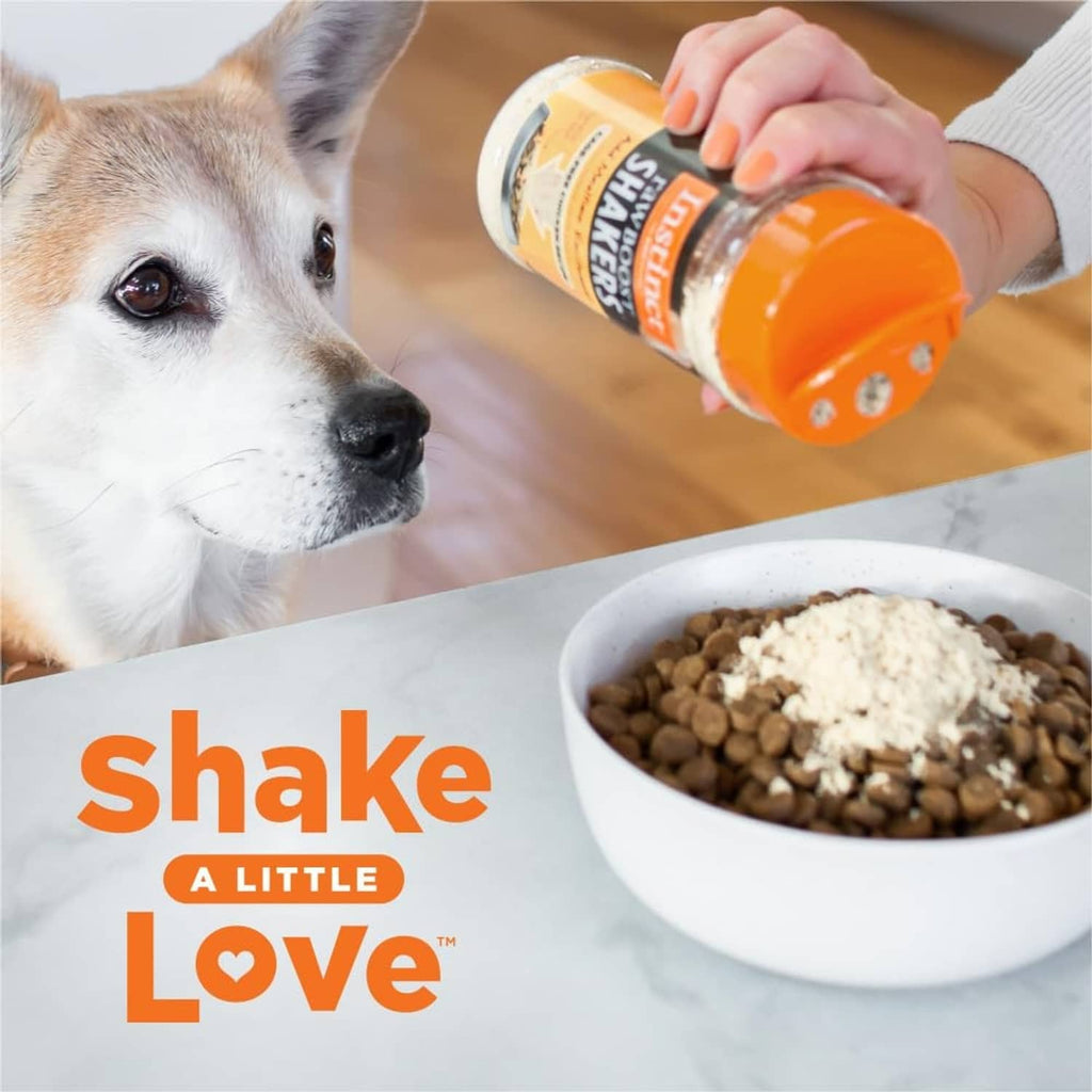 Dog receiving Instinct RawBoost Shakers from an orange shaker jar with a bowl of topper