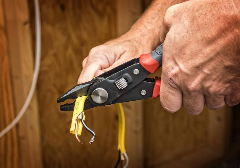 Hand using lineman’s pliers to strip yellow wire; black handle with orange accents.