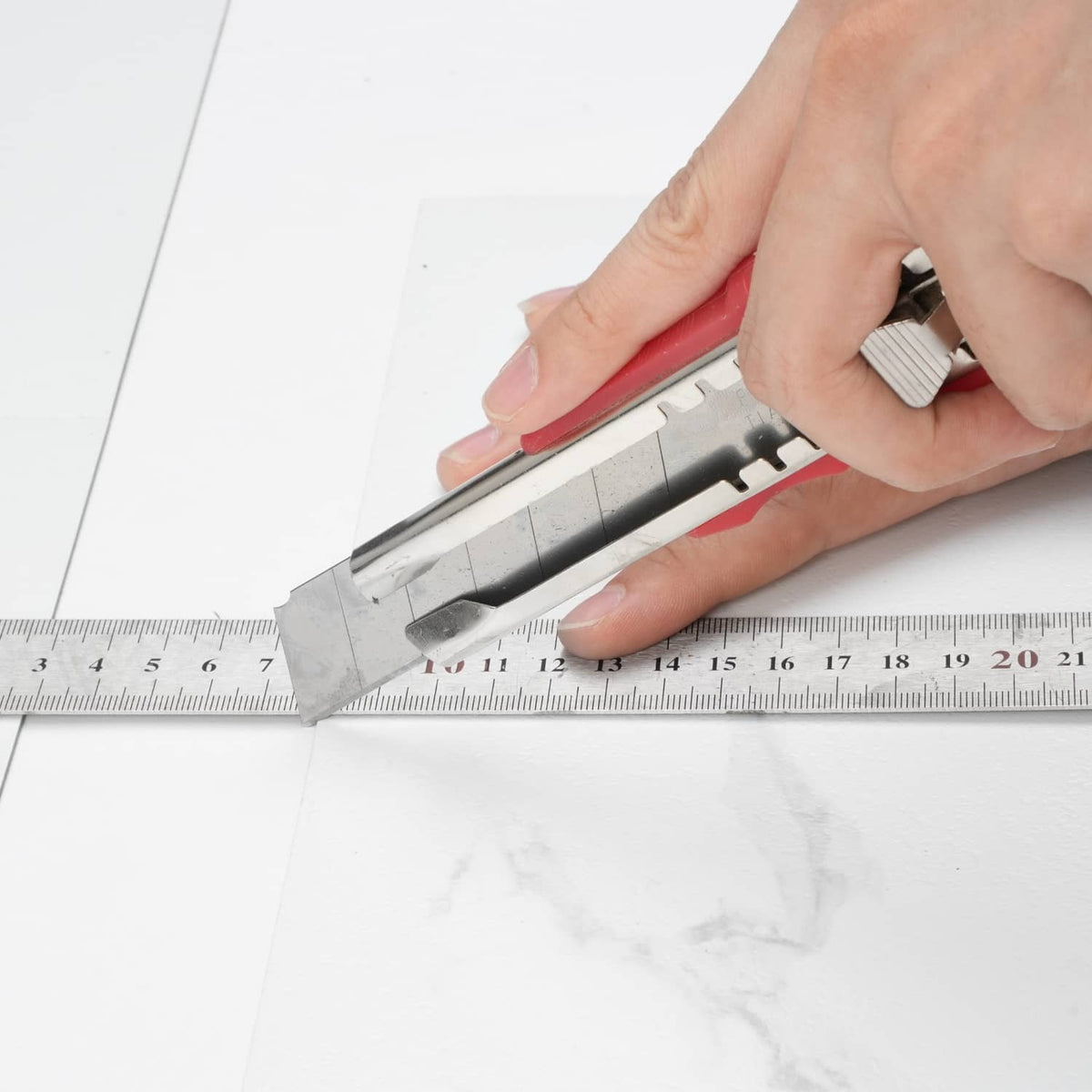 Hand trims a white marble-pattern self-adhesive vinyl tile using a cutter and ruler