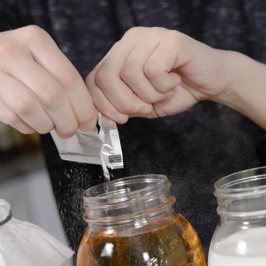 Hand pouring freeze-dried kefir starter powder from foil packet into jar