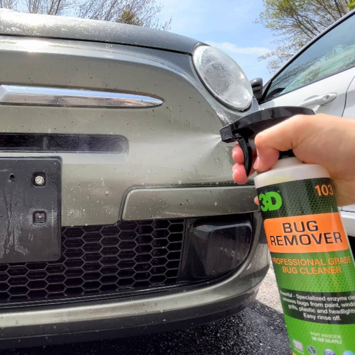 Hand applying 3D bug remover cleaner to a car front; orange bottle with black sprayer
