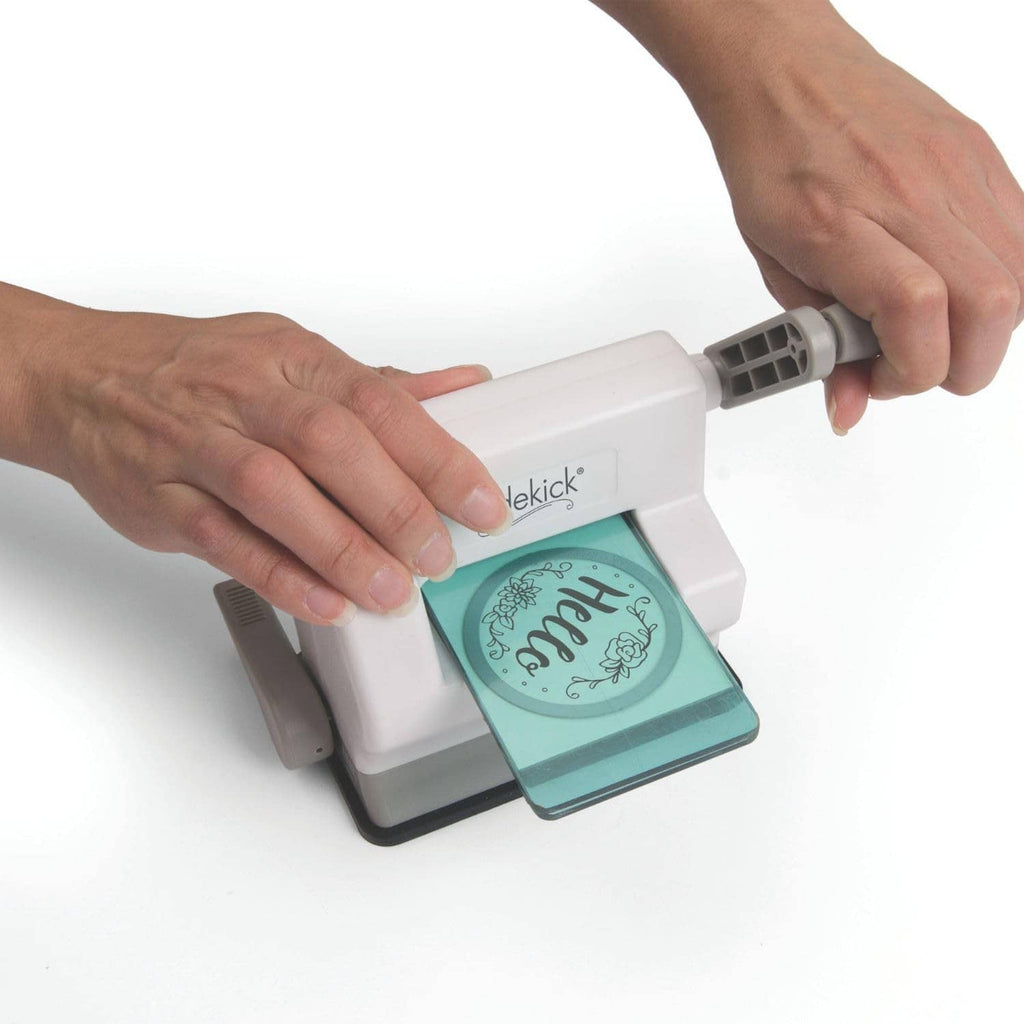 Hands operating white die-cutting machine with teal plate and embossed design