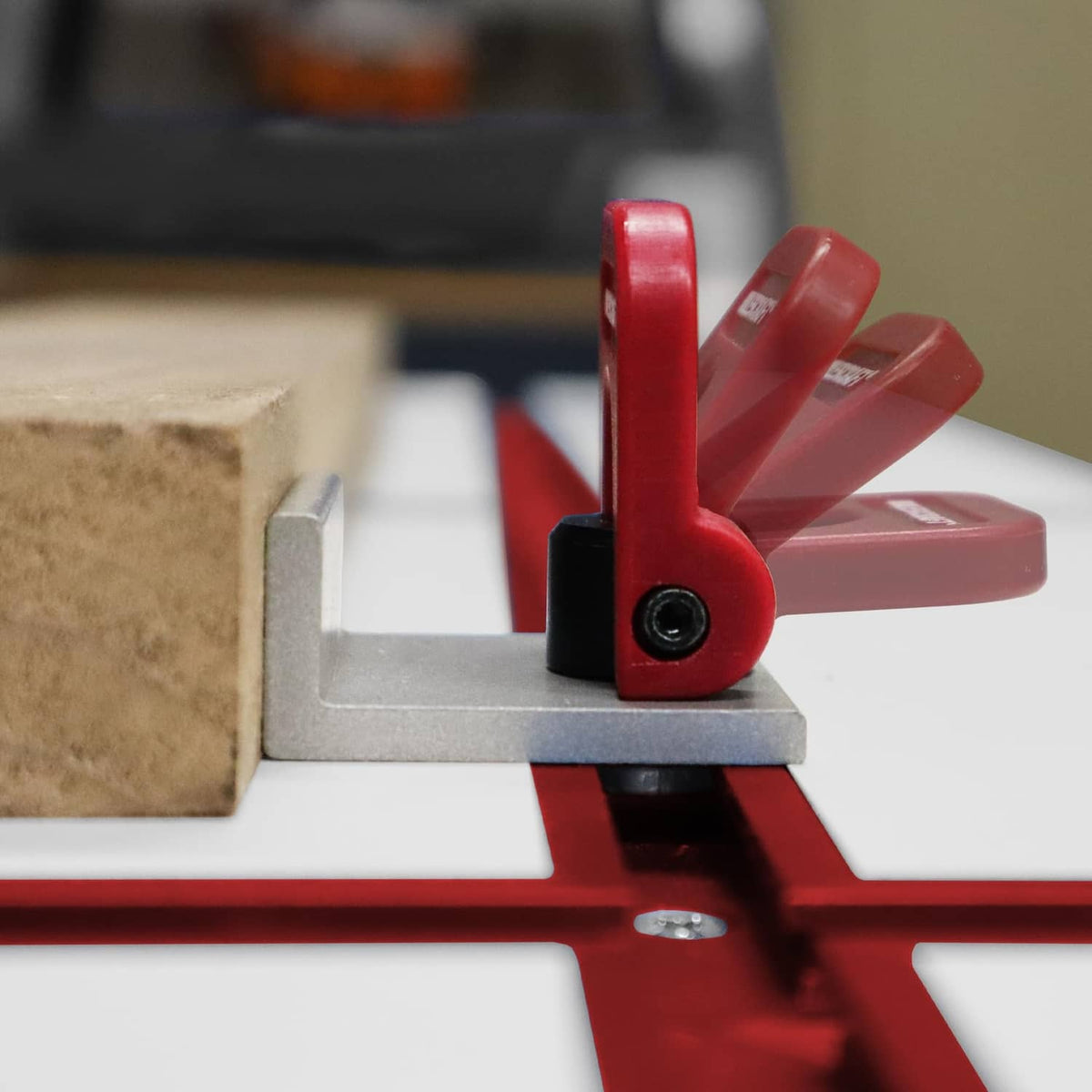 Red cam stop clamp with black knob on T-track, holding a wood panel edge