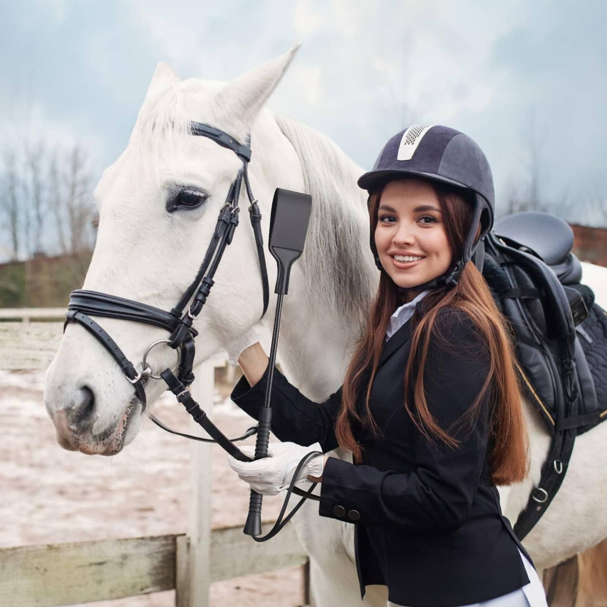 Black riding crop in rider’s hand near horse tack, with wrist strap