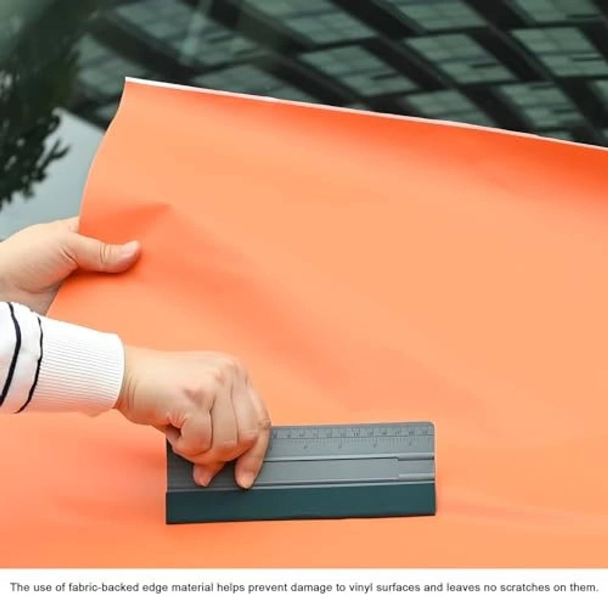 Hand using felt squeegee applicator with ruler on orange vinyl film