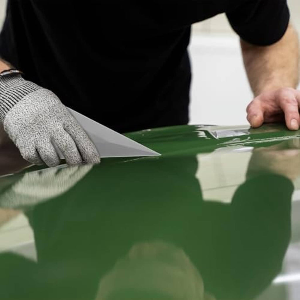 Gloved hand pressing a gray triangle window tint squeegee card on glass