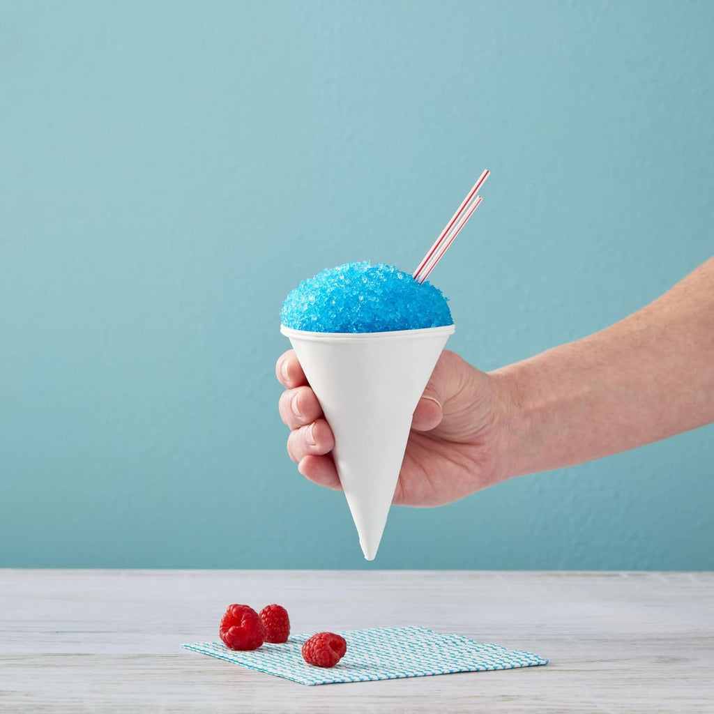 Hand holding white cone cup with blue slush, red raspberries on table