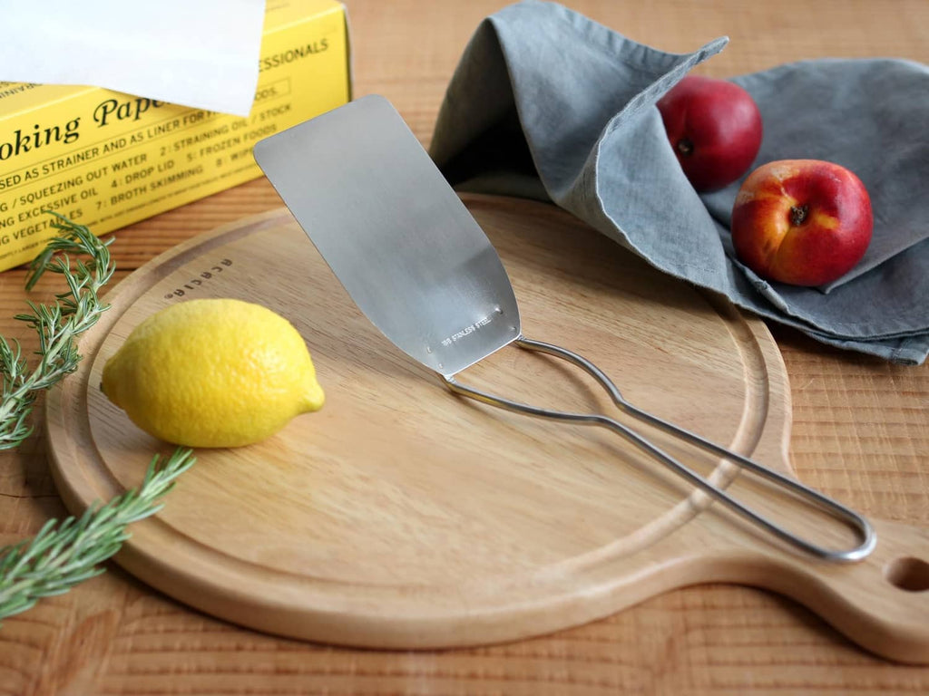 Stainless steel cookie spatula with flat blade and arched handle on a wooden board
