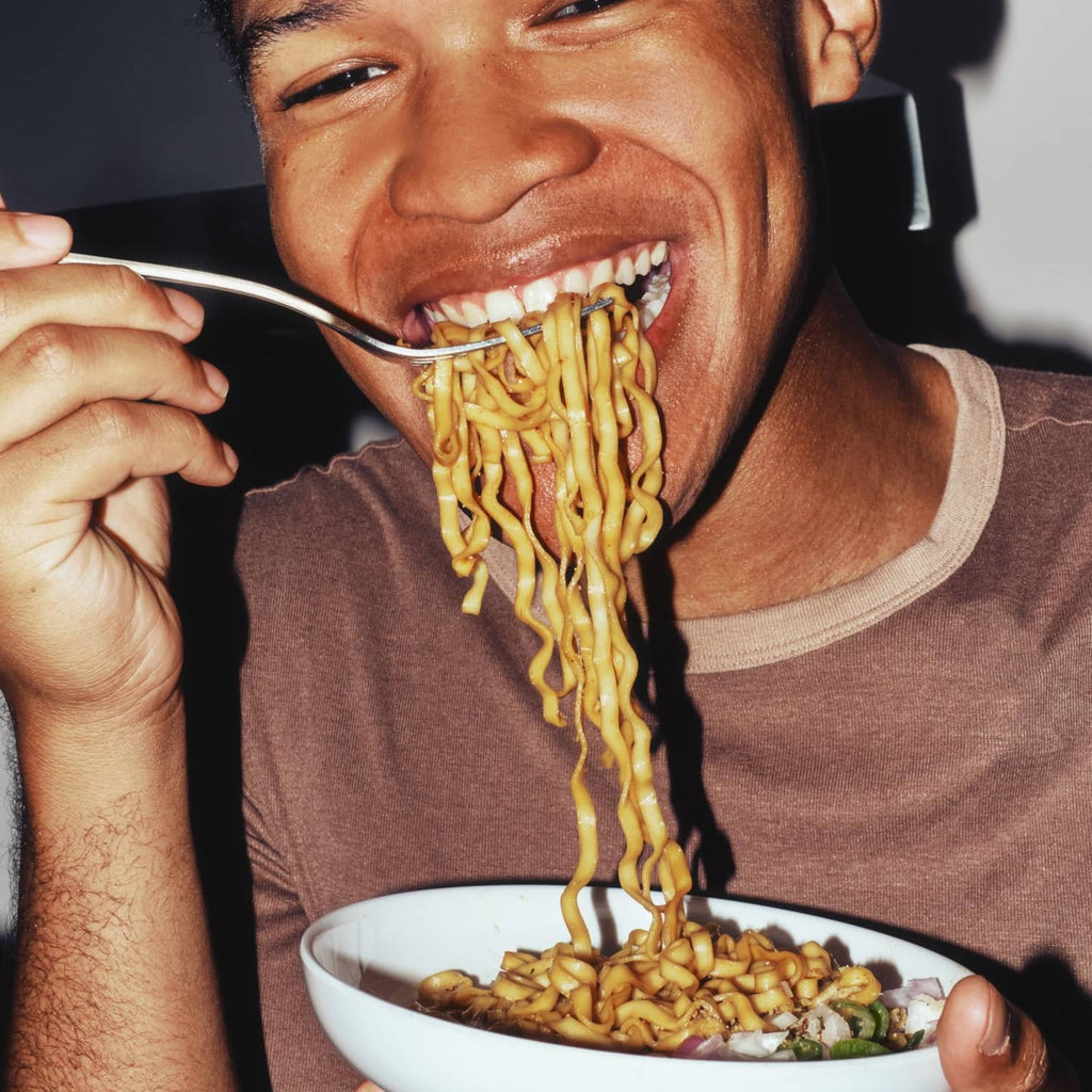 Person eating soy and scallion ramen noodles with a spoon and bowl