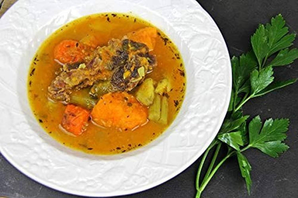 Bowled soup with vegetables and herbs, golden broth in a white plate