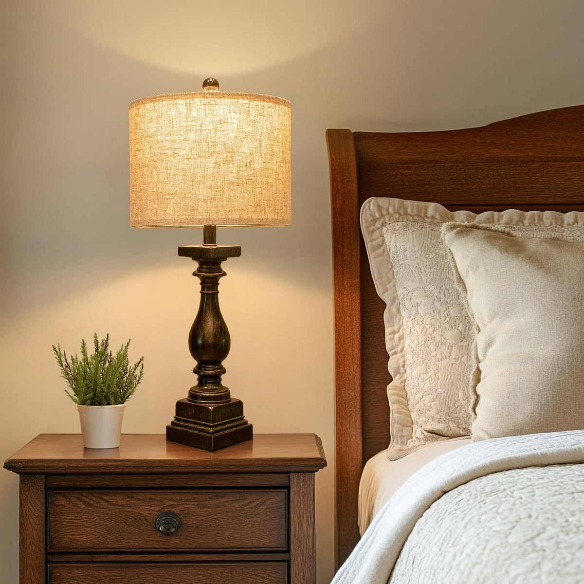 Table lamp with beige drum shade and dark turned base beside bed, cable visible