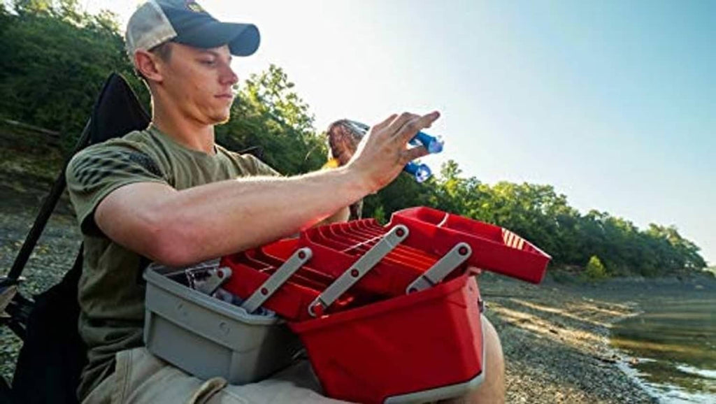 Red and gray tackle box held on a riverside, with carry handle visible
