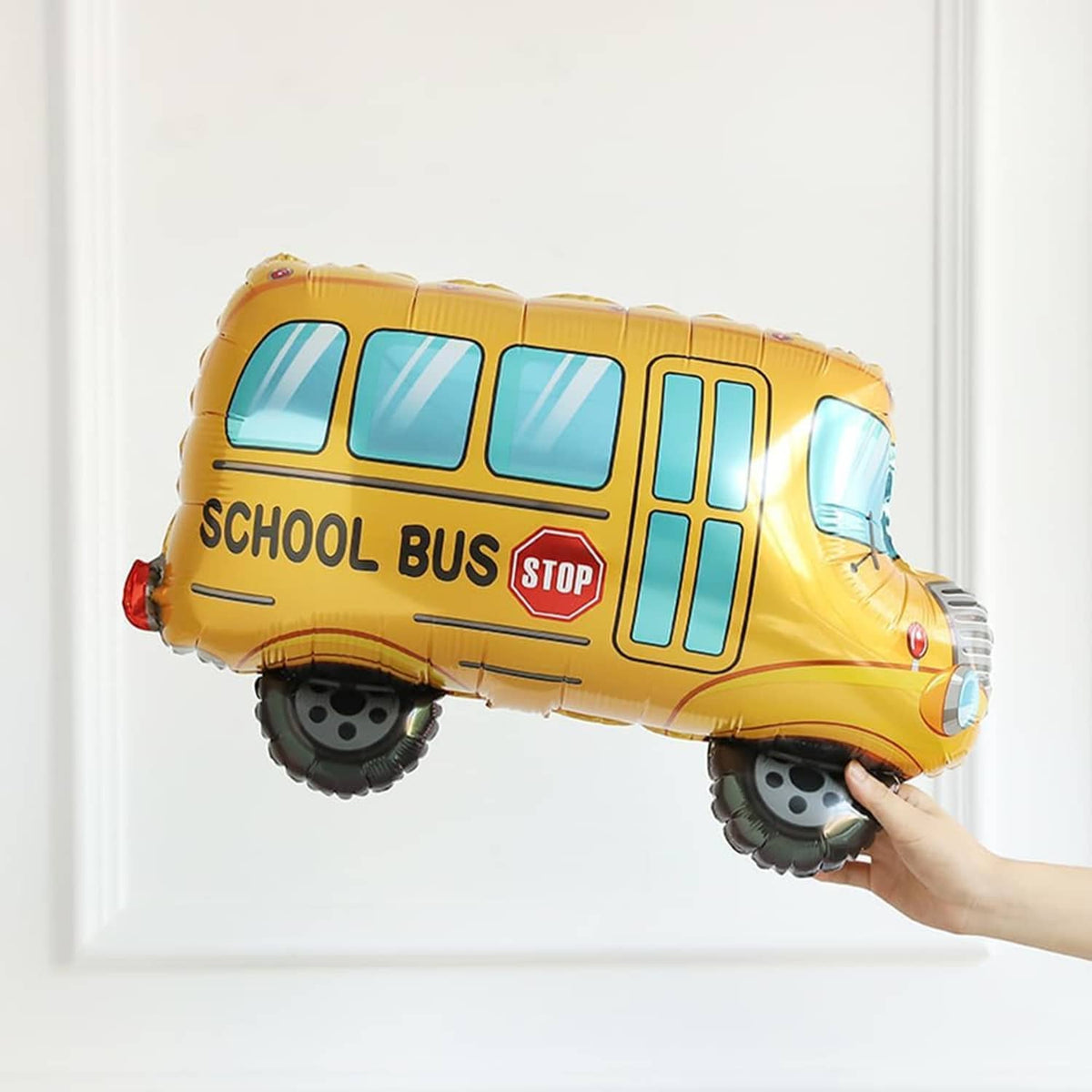 Yellow school bus balloon with blue windows and stop sign, held in a hand