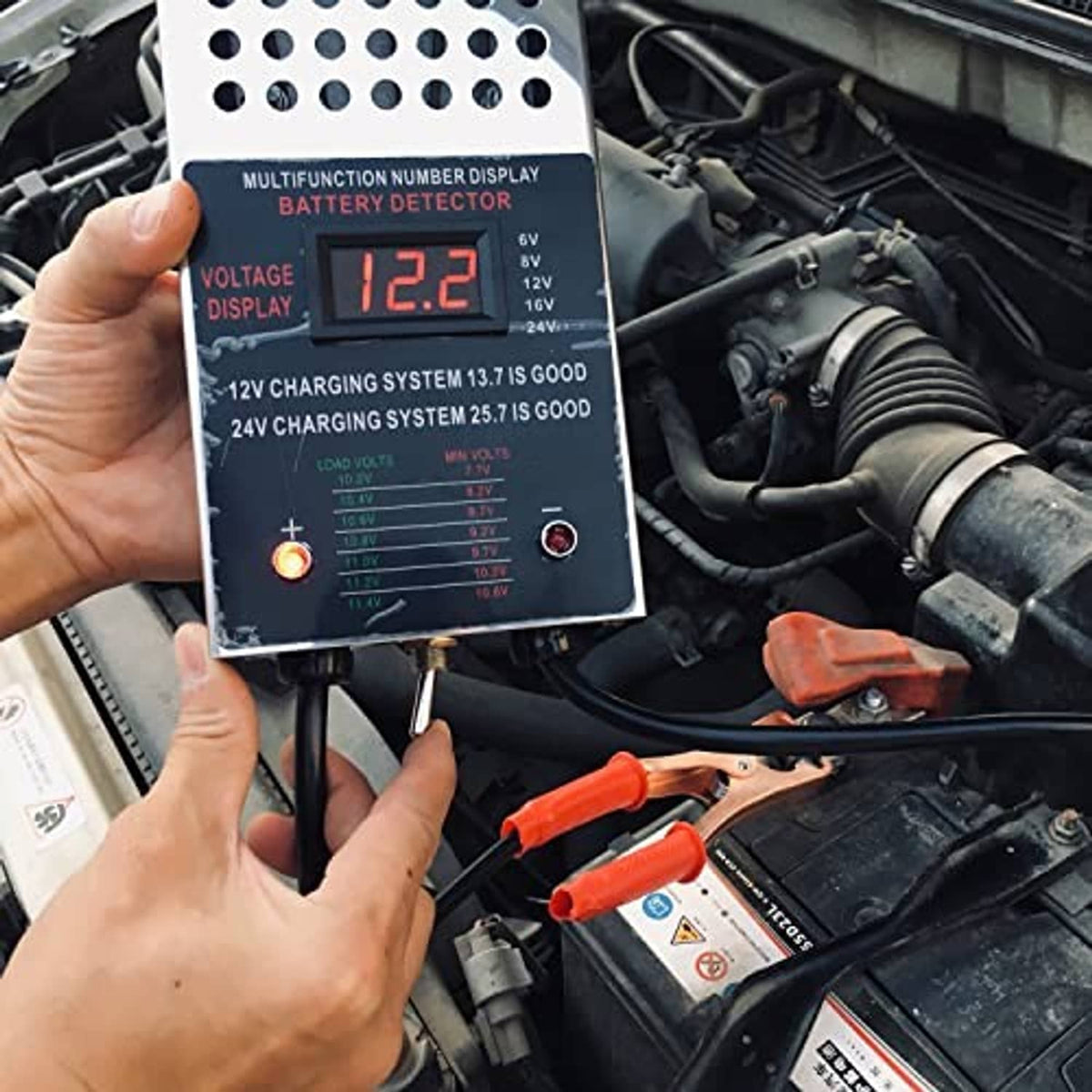 Battery load tester LCD reading 12.2 V, with connected clamp leads on the panel