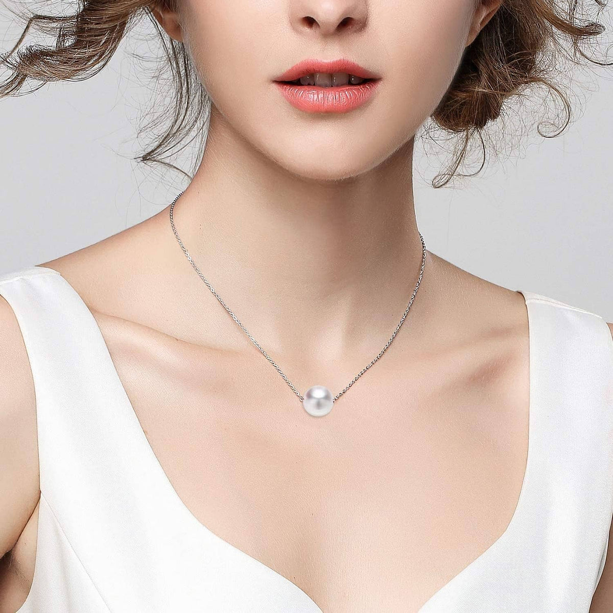 Silver-plated necklace chain with a single round pearl pendant worn at neckline.