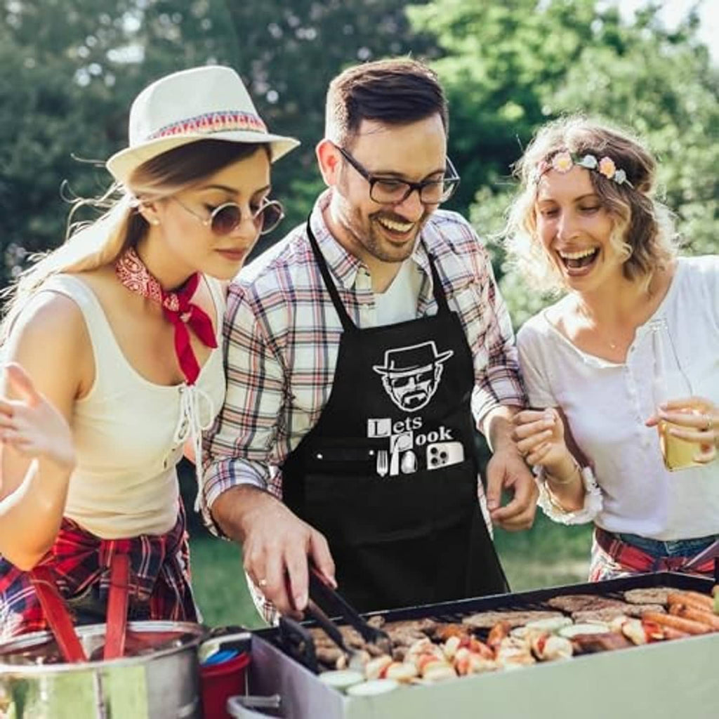 Black 'Lets Cook' apron worn while grilling; chef-face logo over the chest
