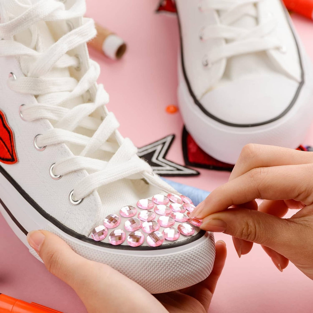 Acrylic teardrop gems being applied to a white sneaker near the toe