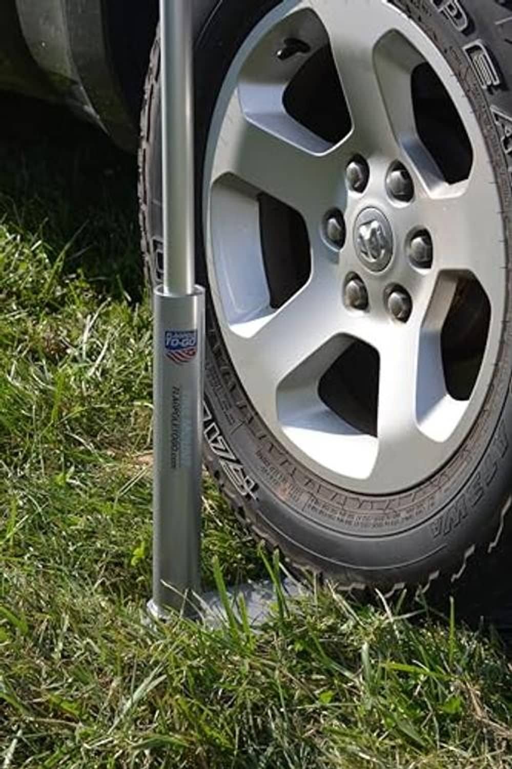 Upright flagpole post with silver base near car wheel and tire