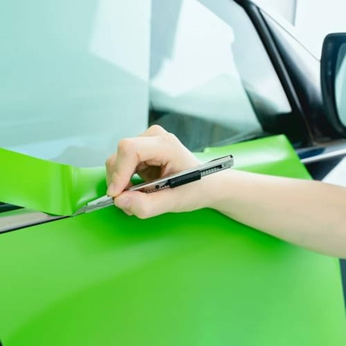 Hands using a squeegee tool to apply neon green window tint film