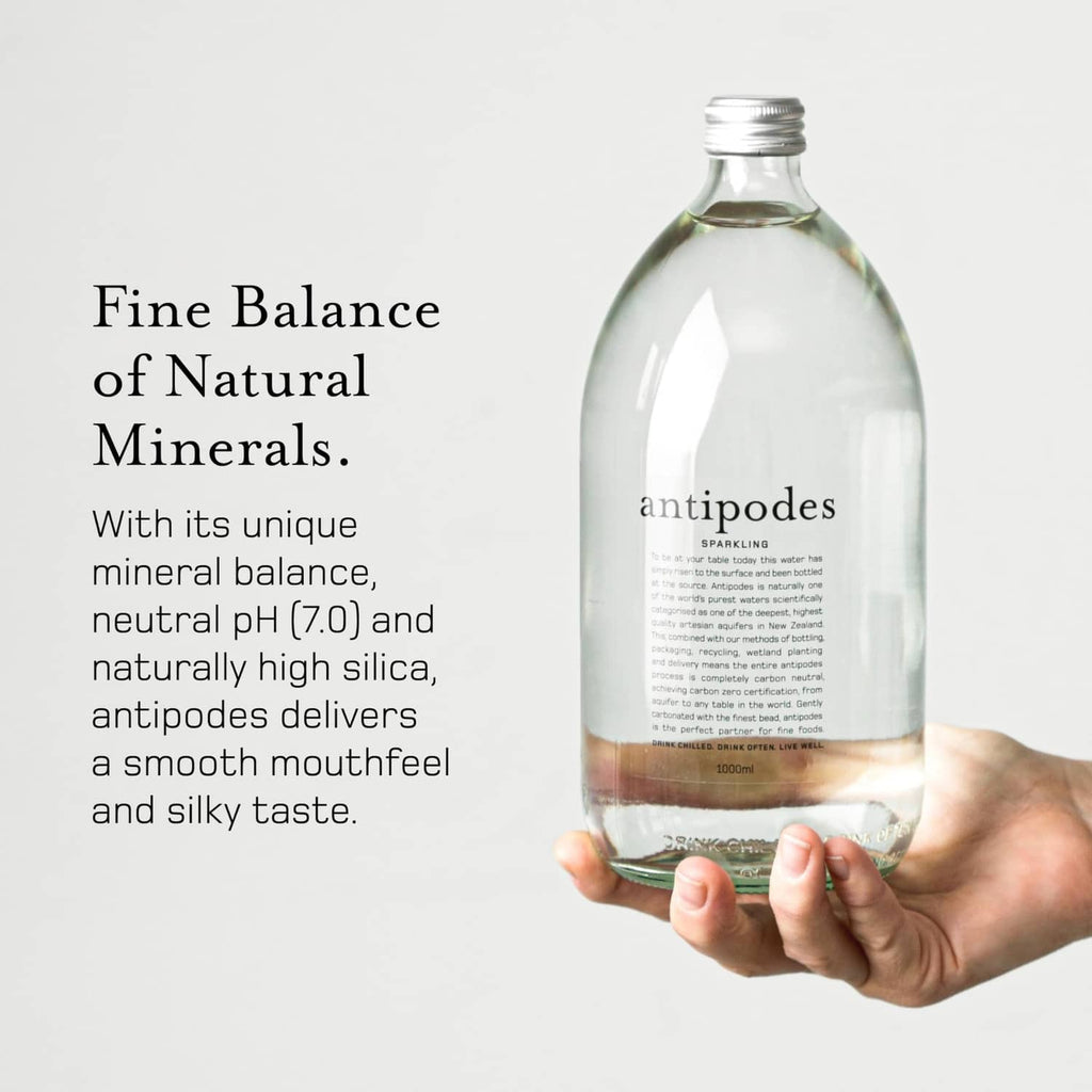 Hand holding Antipodes sparkling artesian water bottle, clear glass with front label