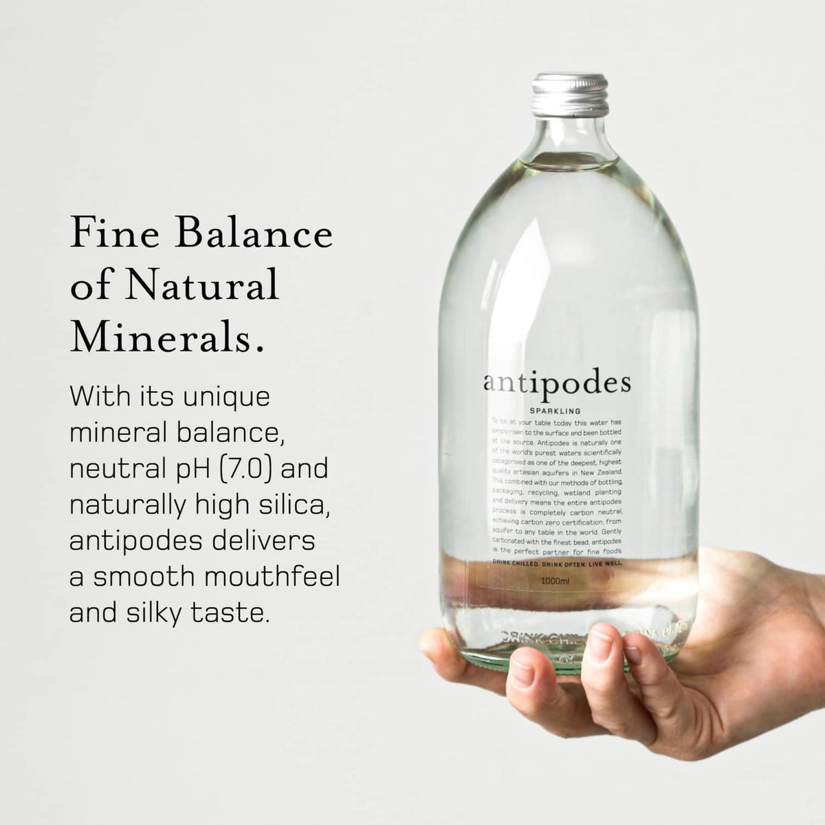 Hand holding Antipodes sparkling artesian water bottle, clear glass with front label