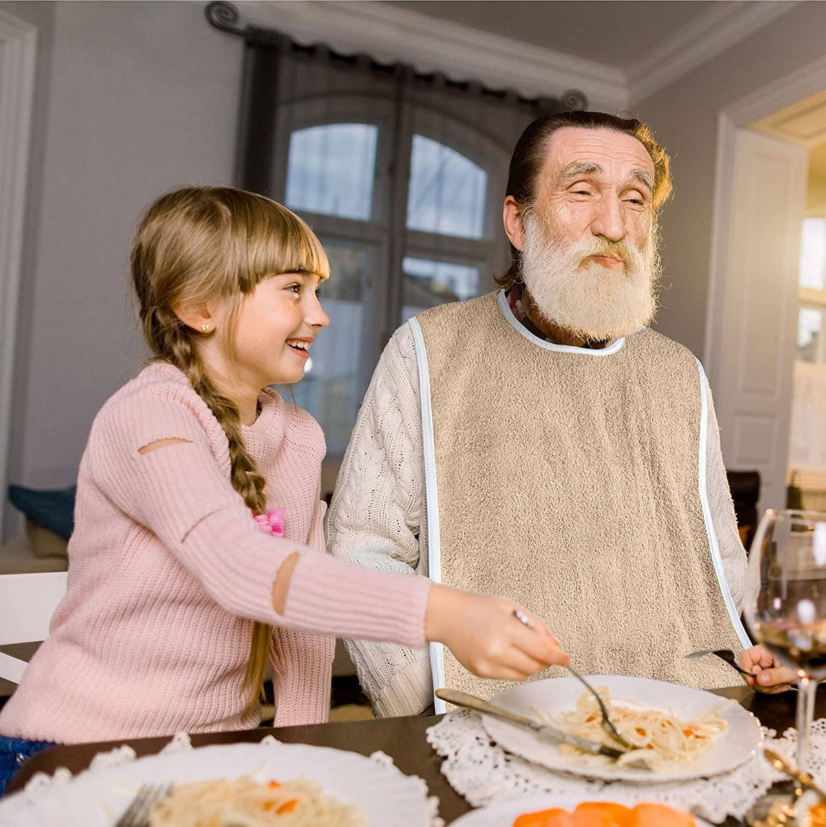 Beige terrycloth adult bib with white edging, worn over clothing during a meal.