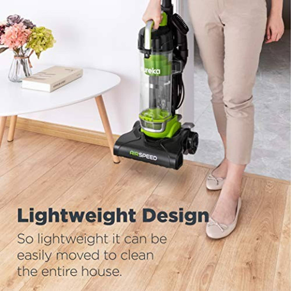 Green bagless upright vacuum cleaner used on hardwood floor beside standing person