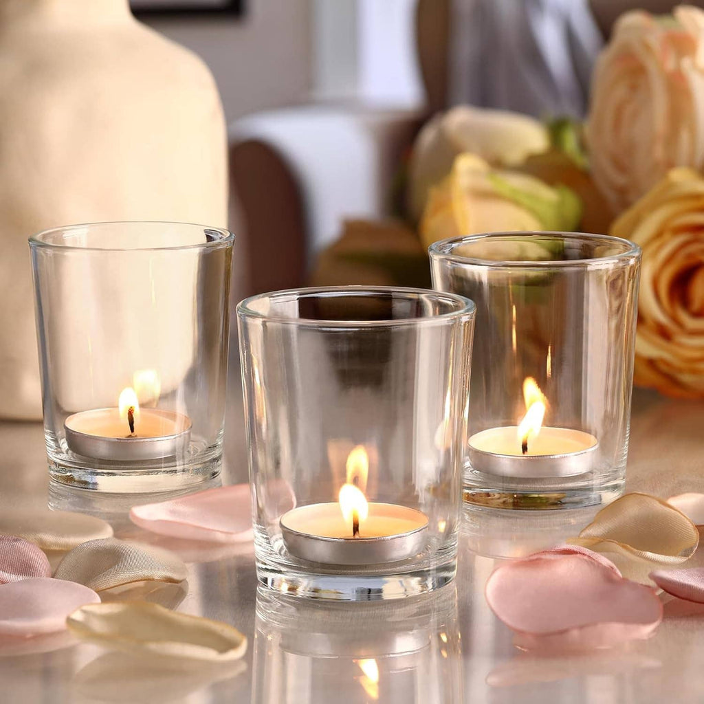 Three clear glass candle holders with lit tea lights on a soft fabric table setting