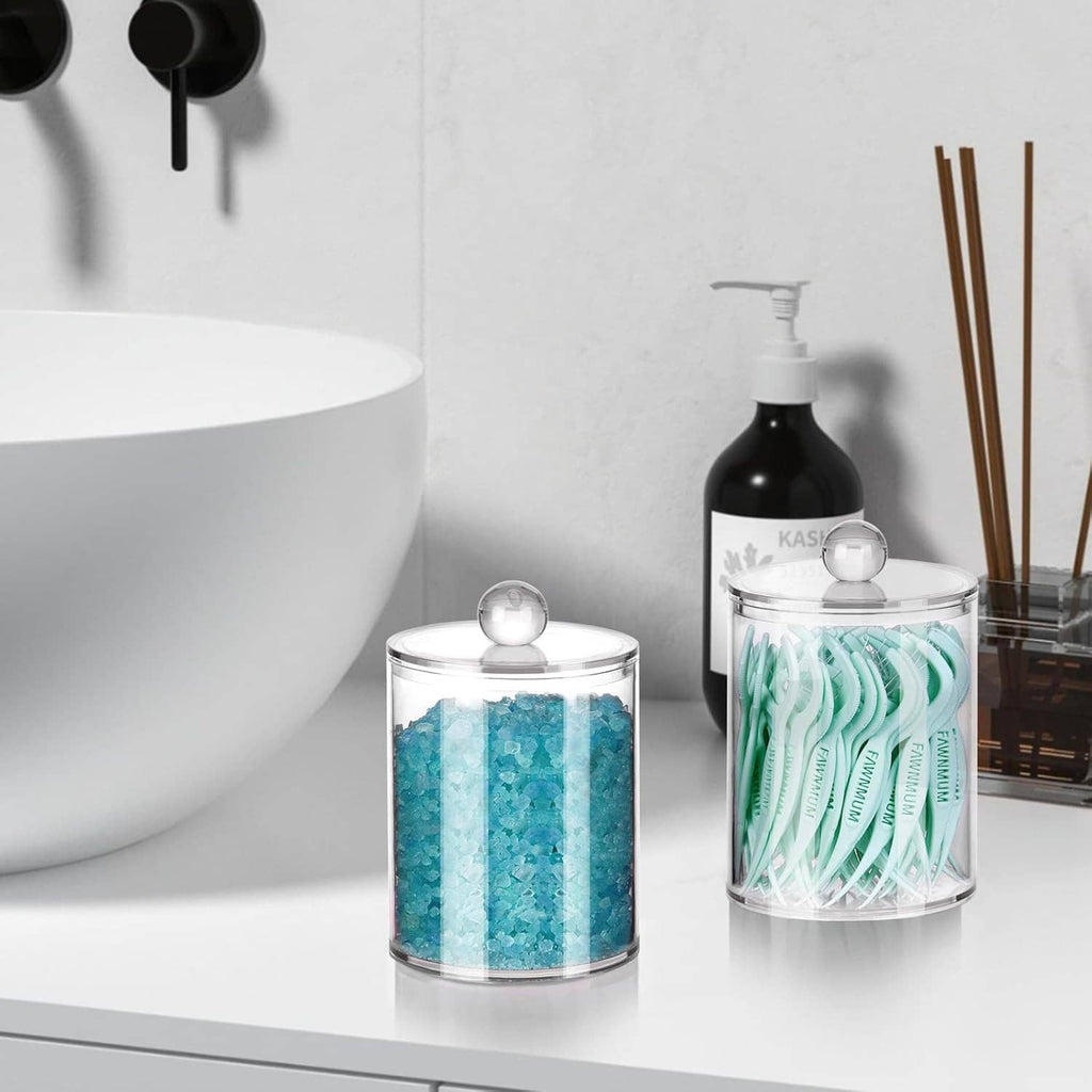 Clear lidded storage jars holding teal and white bathroom cotton accessories on countertop