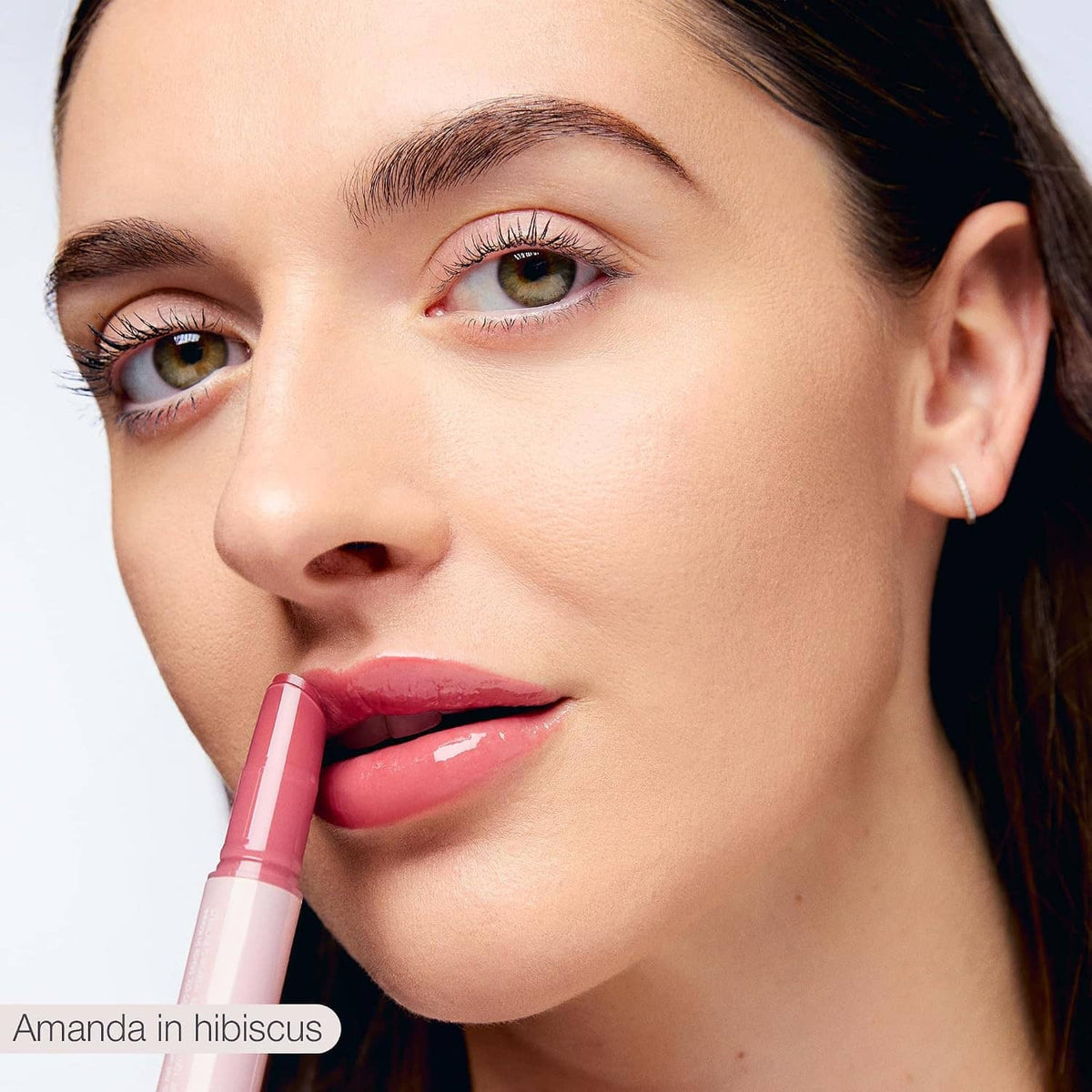 Woman applying Maracuja juicy lip balm on lips, glossy pink tint
