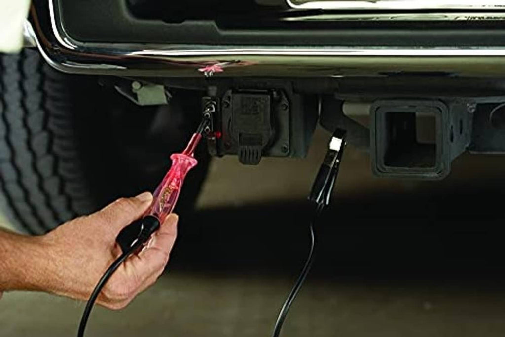 Hand holding circuit tester at vehicle battery terminals with probe and clips