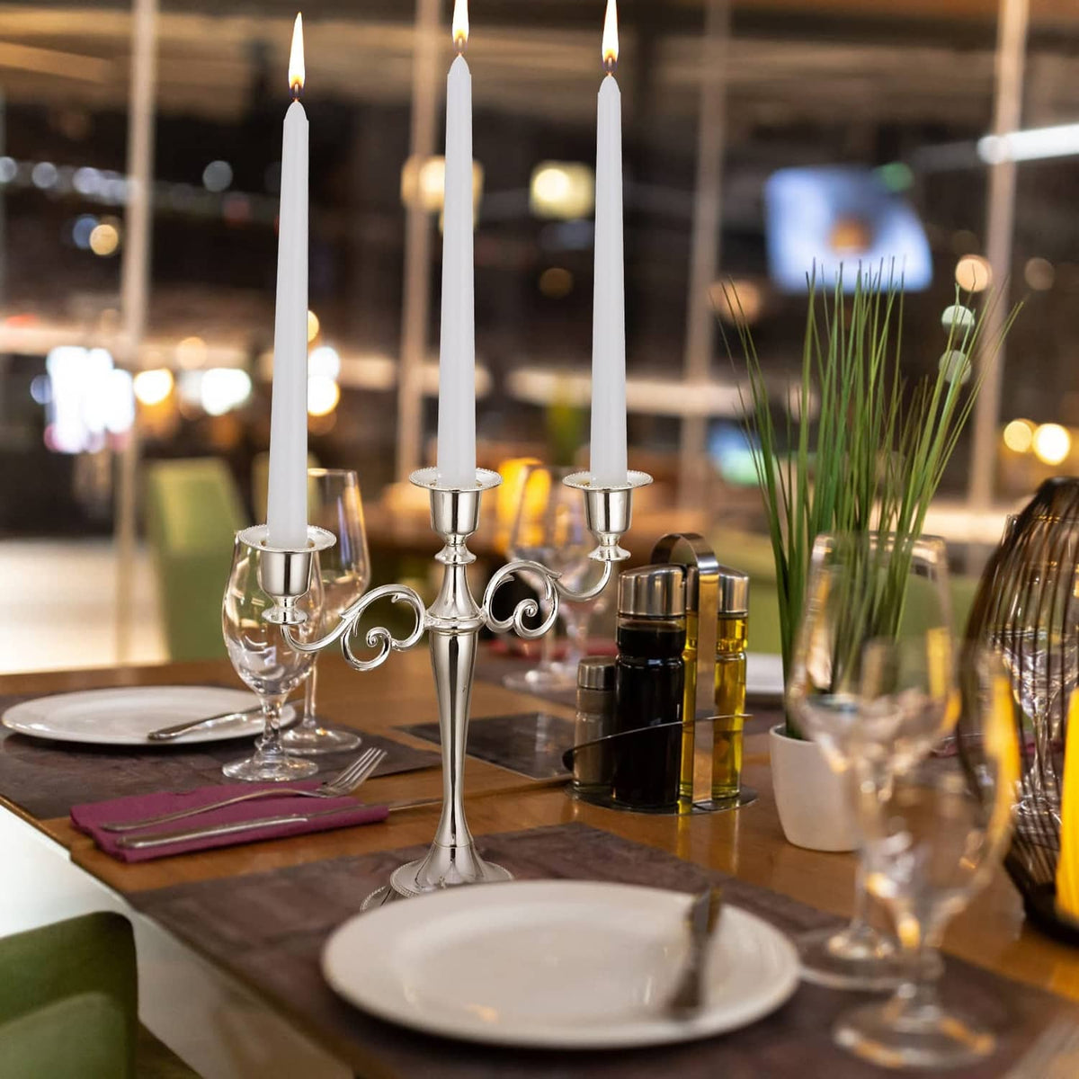 White taper candles in candelabra, lit flames, slender dripless tapers on table