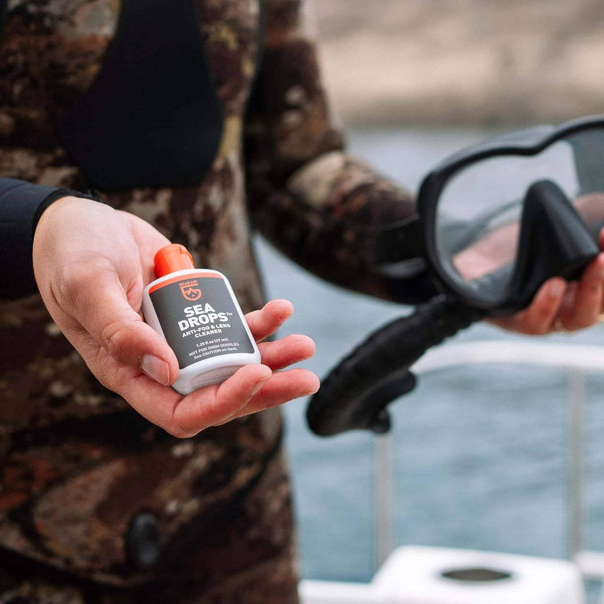 Anti-fog lens cleaner bottle held next to clear swim goggles