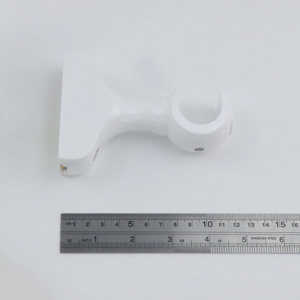 White curtain rod bracket with mounting hole and hook end, measured on ruler