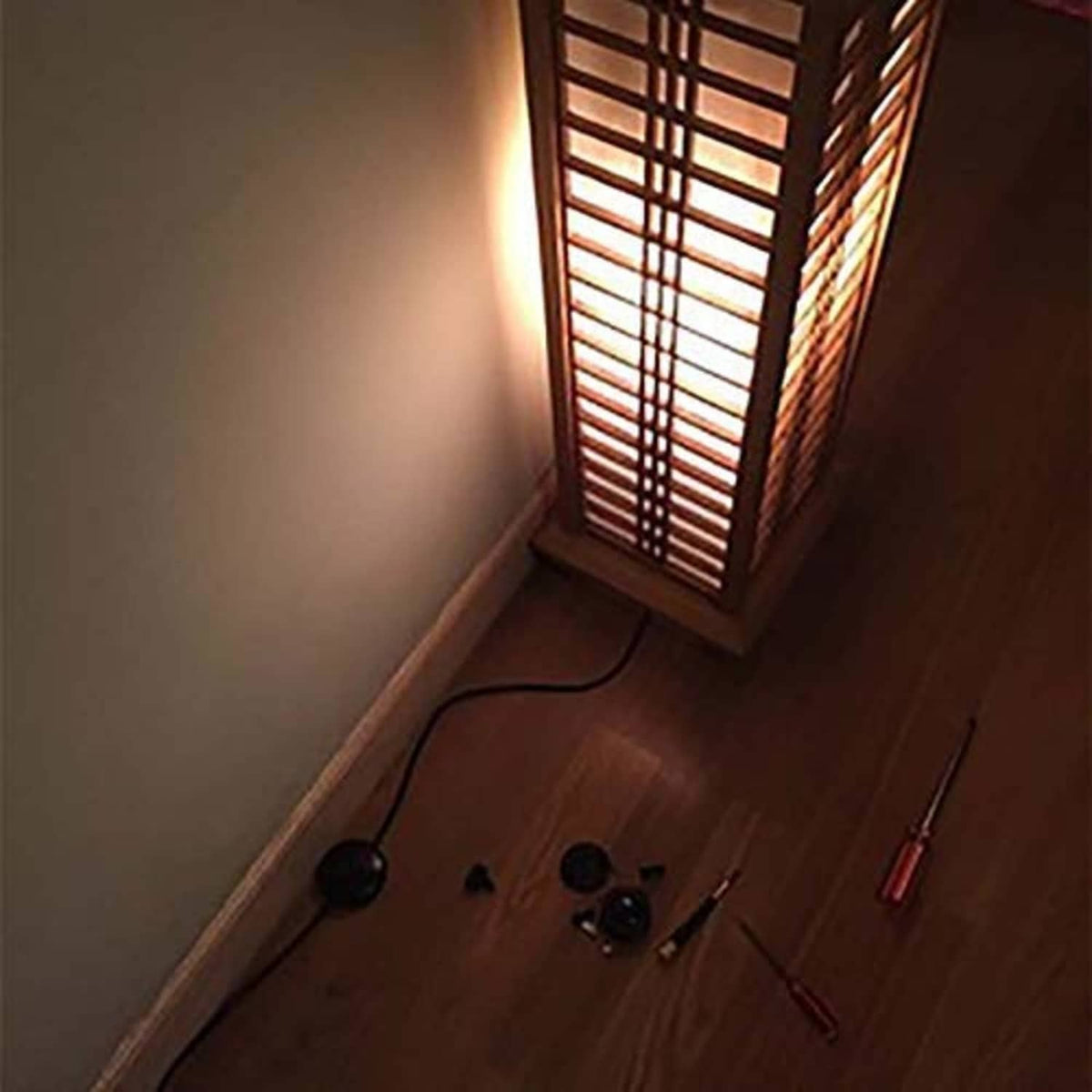 Black round foot pedal lamp switch on the floor with attached cord, near a wall outlet.