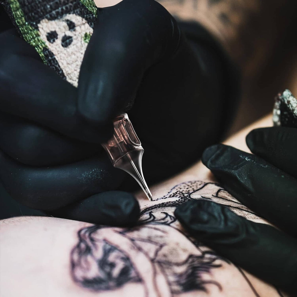 Tattoo artist using a black cartridge pen to ink a detailed design on skin