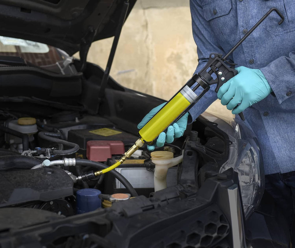 Gloved hand applying yellow UV dye to A/C components using a hose and applicator