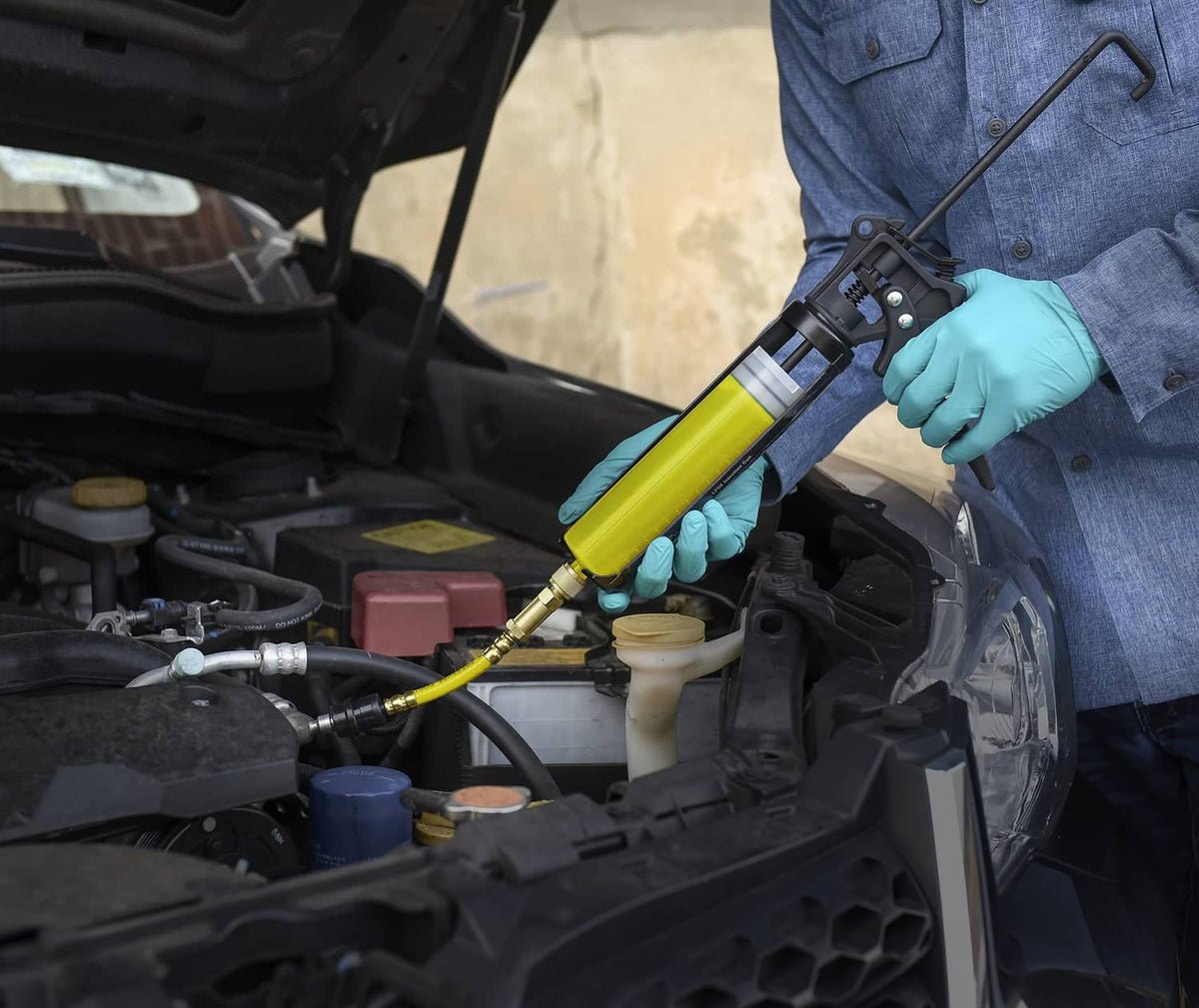 Gloved hand applying yellow UV dye to A/C components using a hose and applicator