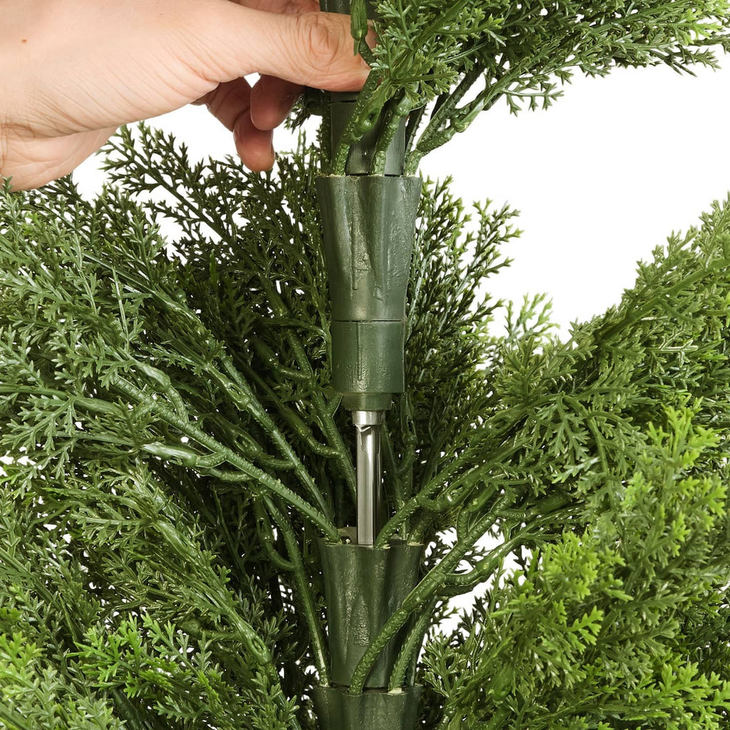Artificial cedar tree with green molded branches and central stem, held by hand