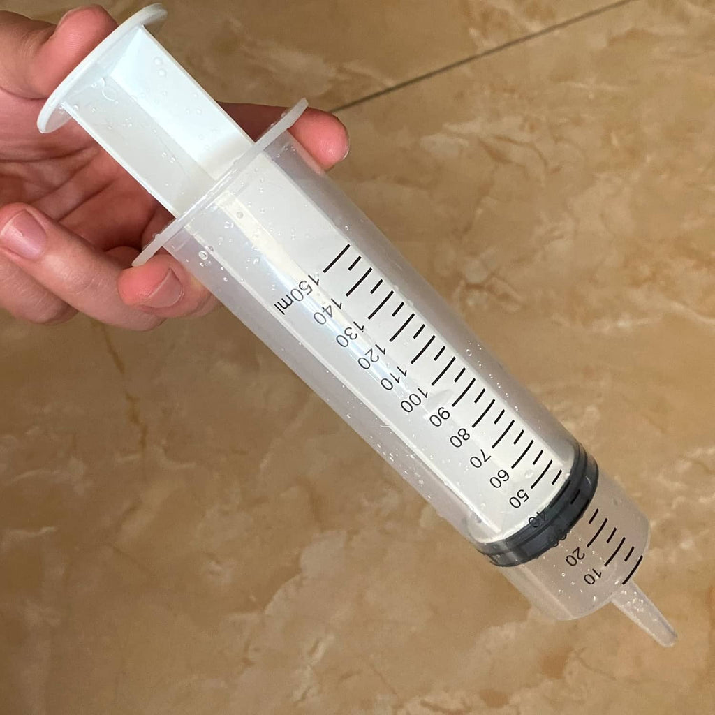 Hand holding clear 150 ml syringe with black measurement scale and gray plunger