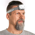 Foxelli LED headlamp flashlight on forehead with dark gray adjustable strap and white housing