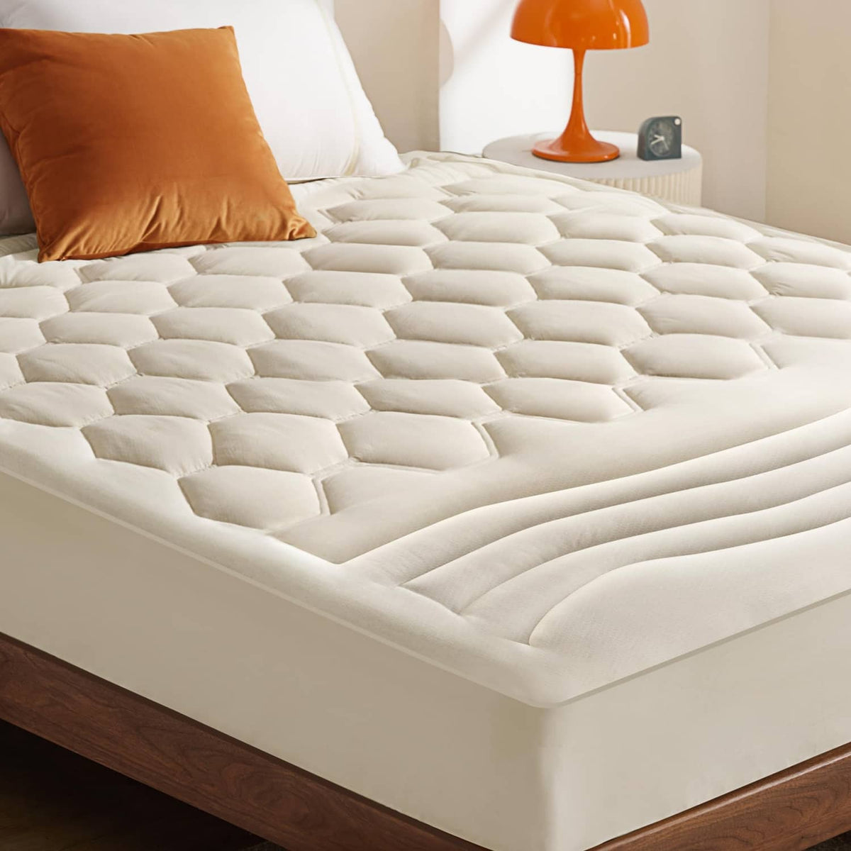 Light beige quilted fitted mattress pad with box-stitch pattern on a bed