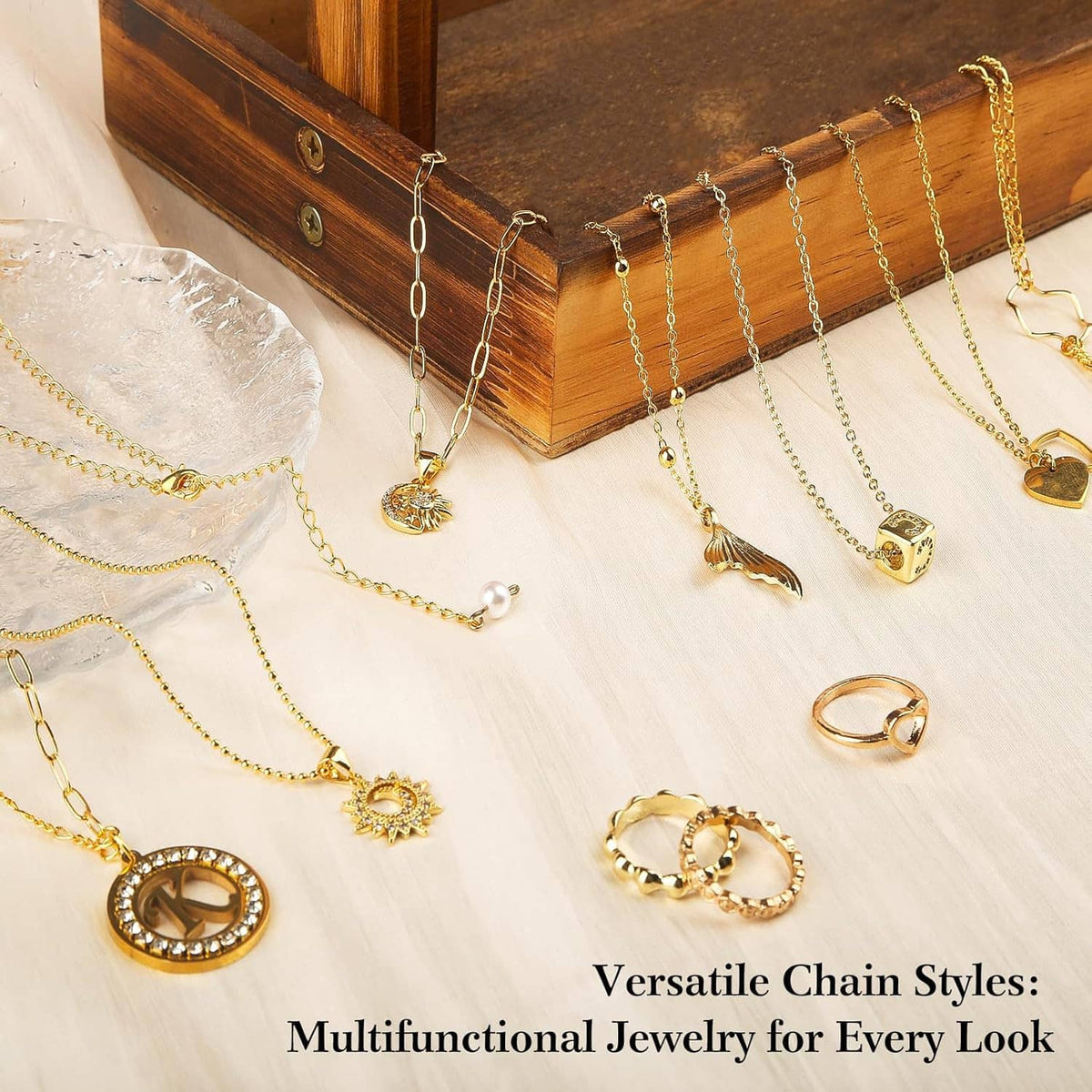 Gold tone charm necklaces and rings laid out on a light wood tabletop