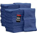 Blue cotton shop towels, stacked in bulk with a hanging “100 pack” tag