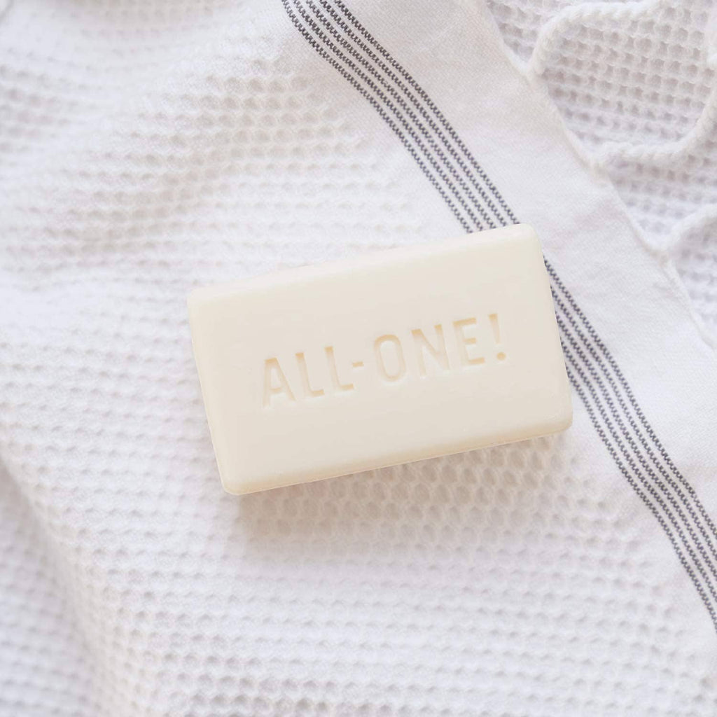 Light cream soap bar labeled ALL ONE on white textured cloth