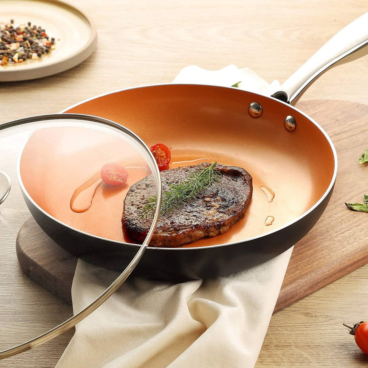 Orange nonstick frying pan with steak and partially covered tempered glass lid, stainless handle